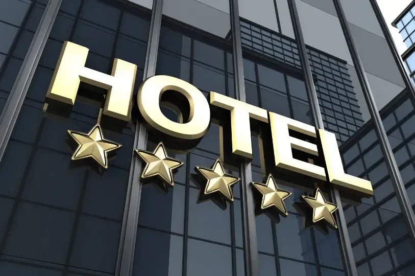 A uniformed hotel bellhop pushes a classic brass luggage cart loaded with bags through a luxurious, 