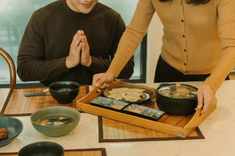 A diner bringing his hands together in a traditional gesture of appreciation before a newly served Japanese meal presented on a wooden tray, reflecting the hospitality and respect inherent in Kyoto's food culture.
