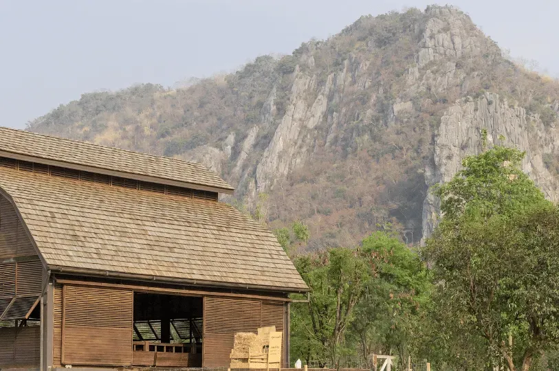 A wooden, barn-style structure with slatted walls and a shingled roof, contrasting with a rugged lim