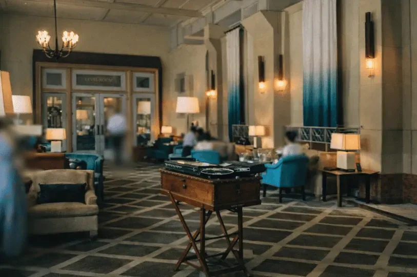 A warmly lit, elegant hotel lobby with a geometric patterned floor. A vintage wooden stand sits in s