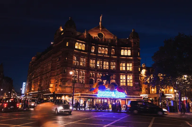 A grand, multi-story theatre building in London brilliantly illuminated at night, featuring a vibran