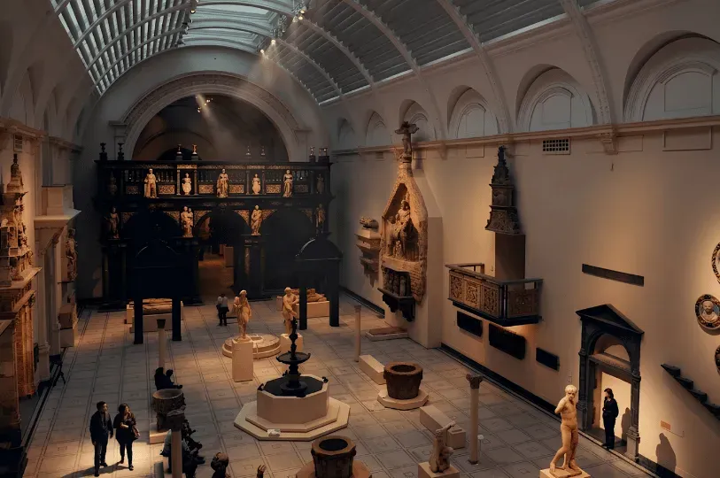 A sweeping view of a grand, high-ceilinged exhibition hall illuminated by natural skylights, filled with classical marble sculptures, architectural fragments, and ancient stone antiquities.