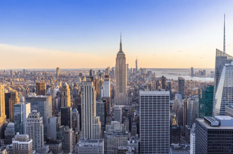 A panoramic, high-angle view of the New York City skyline at golden hour, featuring the Empire State