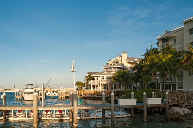 A serene, sunlit waterfront resort featuring a wooden dock with parked jet skis in the foreground. I