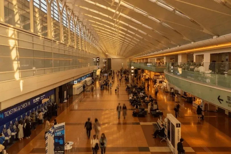 A wide view of a modern Tokyo airport terminal bathed in warm golden-hour sunlight, showing traveler
