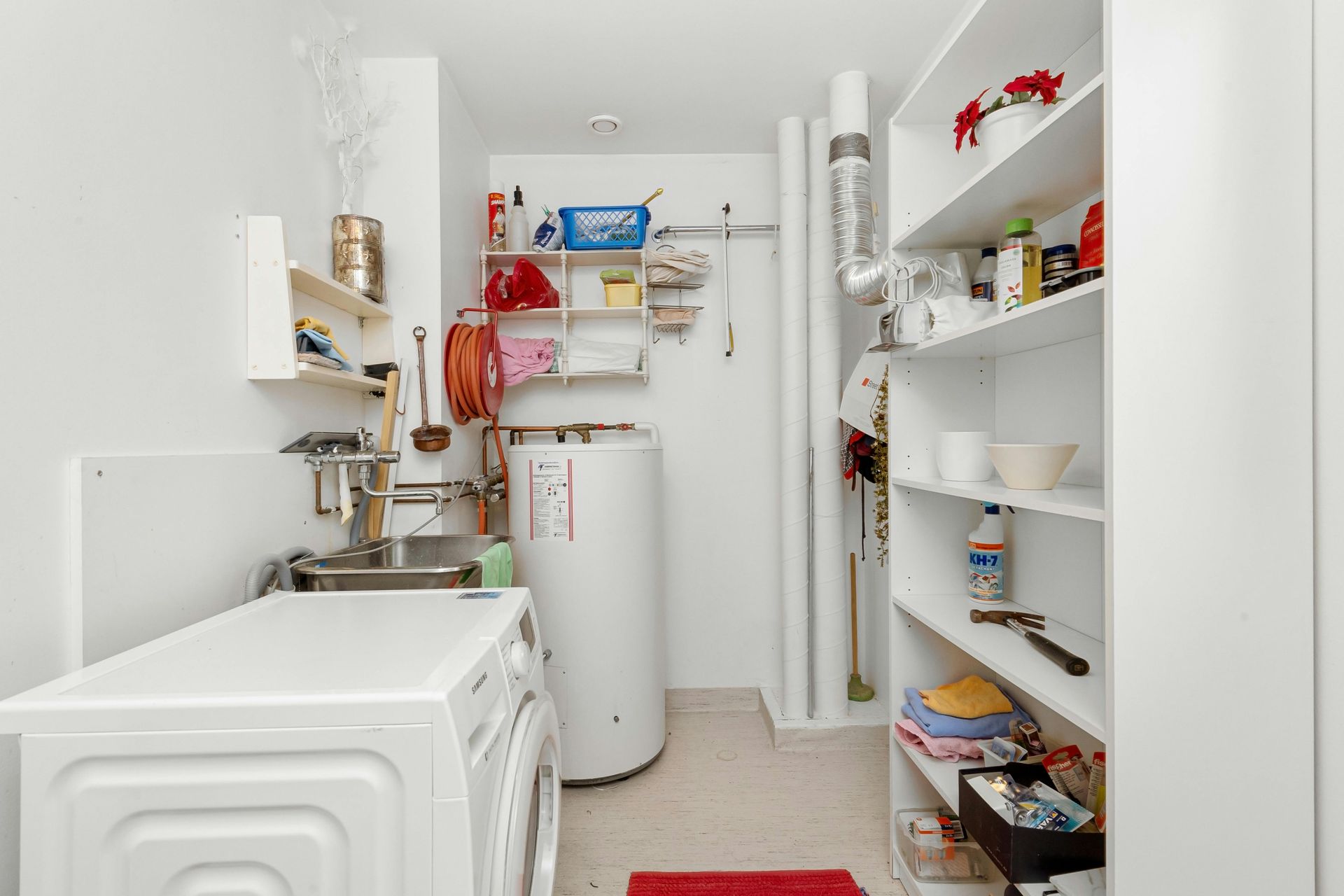 Laundry room with white washer, shelves, and water heater.