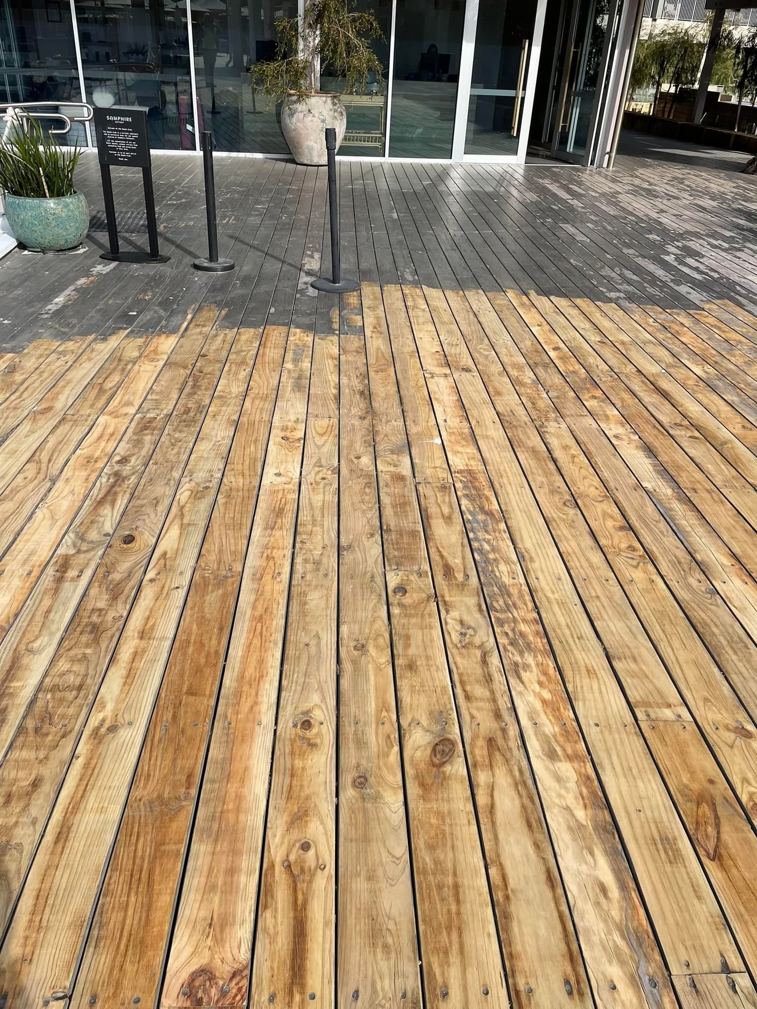 Wooden deck with gray and brown planks, leading to a building with glass doors.