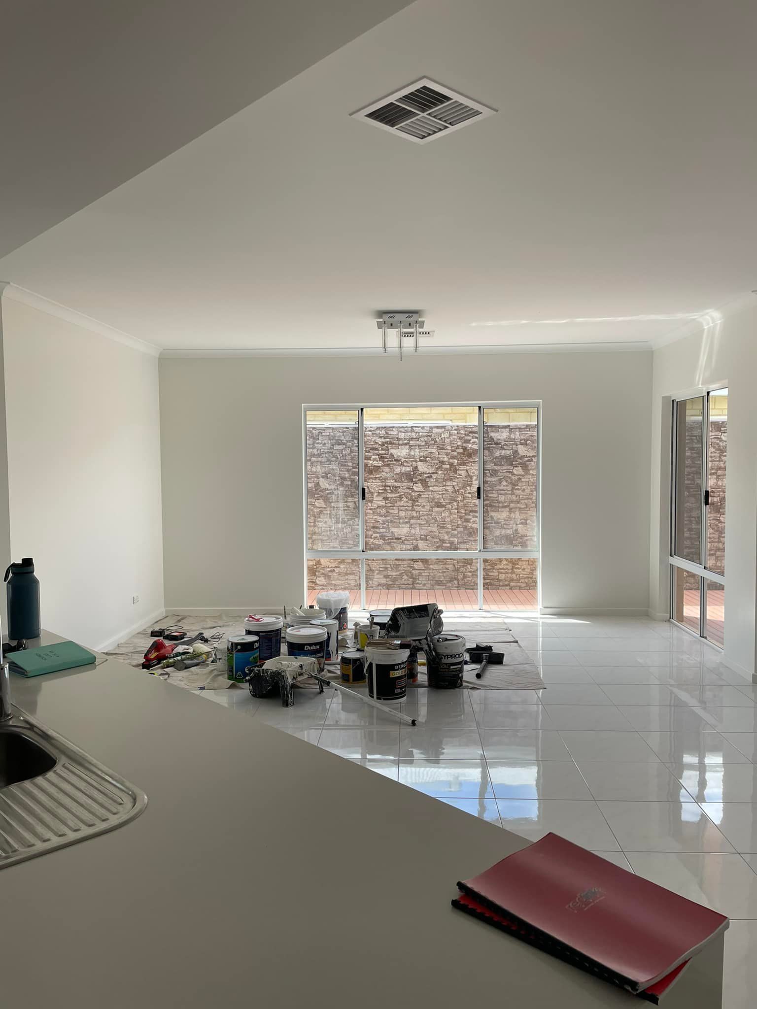 Interior room with paint supplies and new white paint. Large windows and a kitchen countertop are visible.