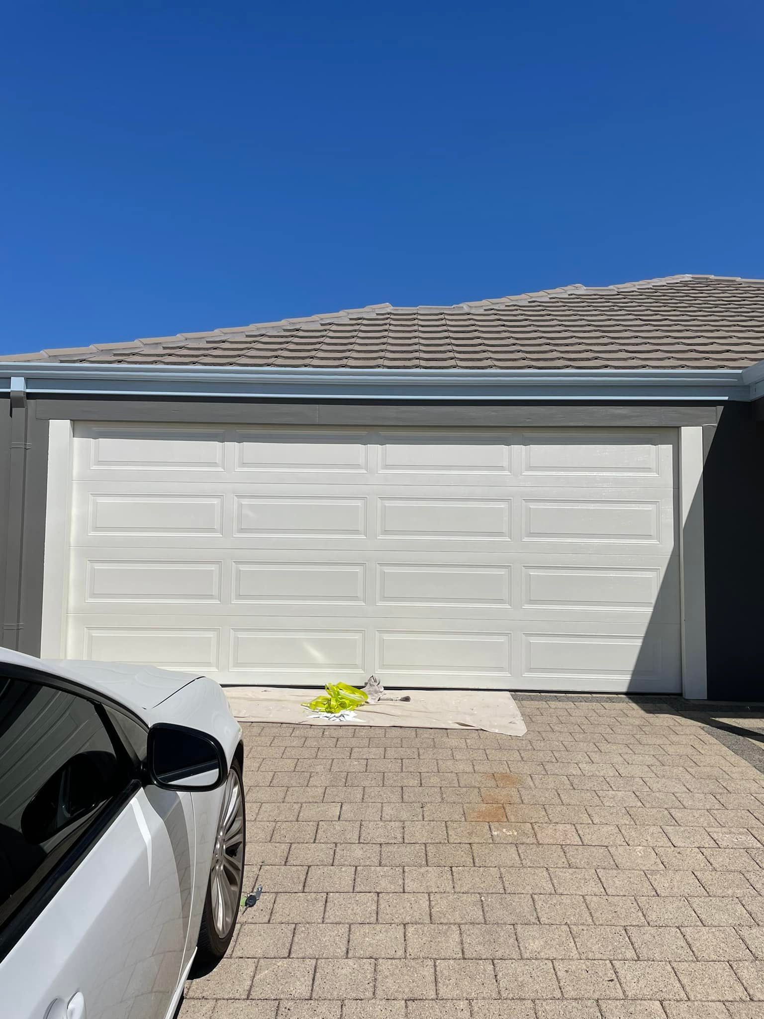 White garage door with car parked in driveway, clear blue sky.