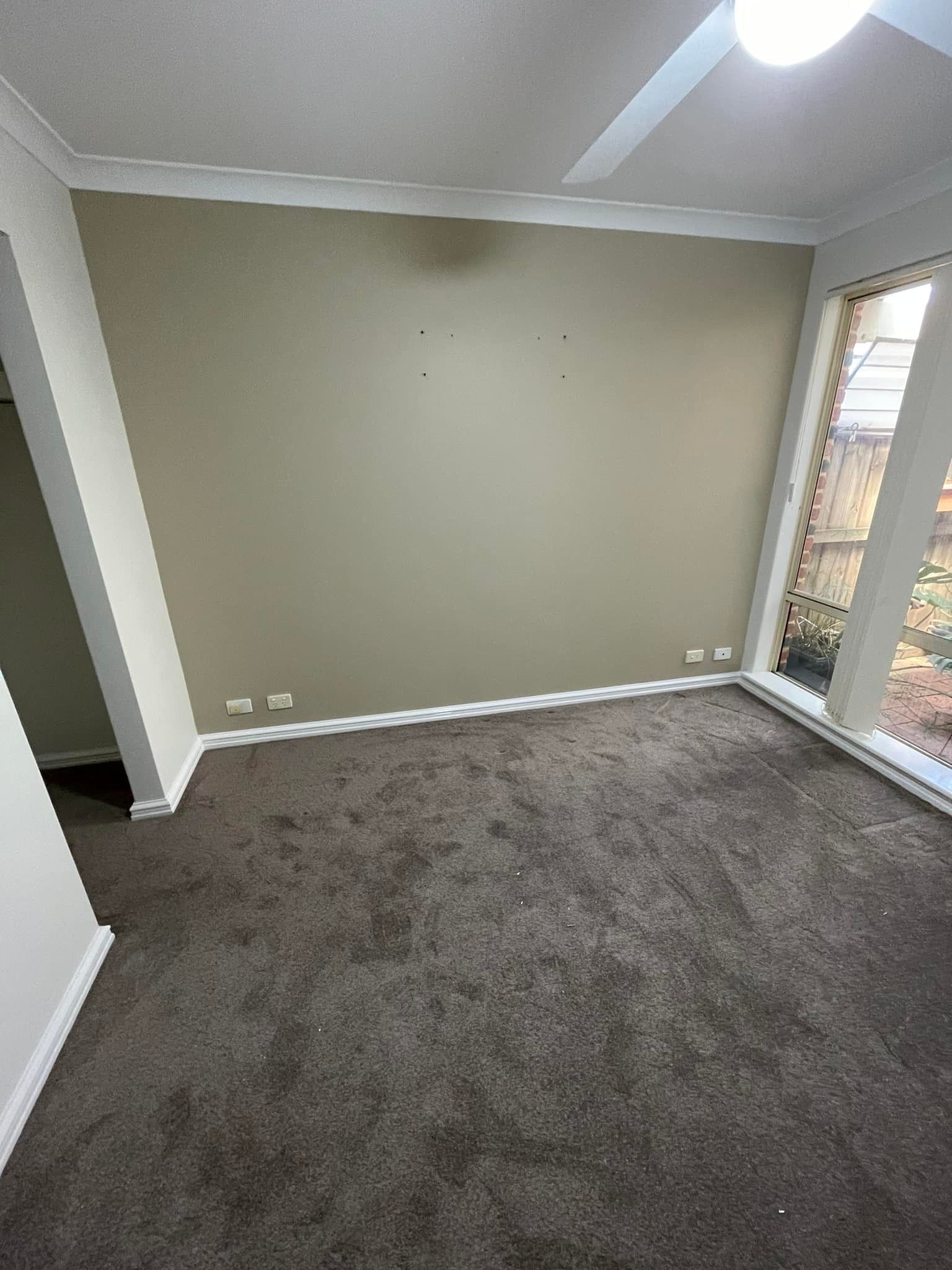 Empty room with beige walls, white trim, and gray carpet. Large window on the right.