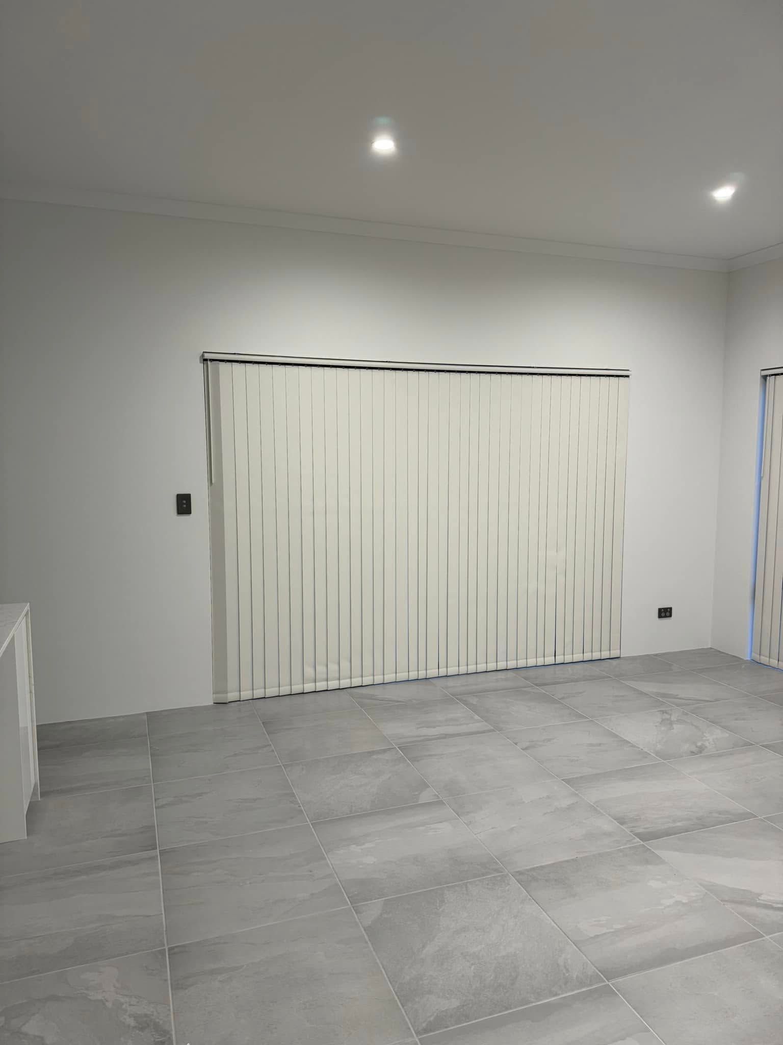 Room with white walls, tiled floor, and vertical blinds covering a window.