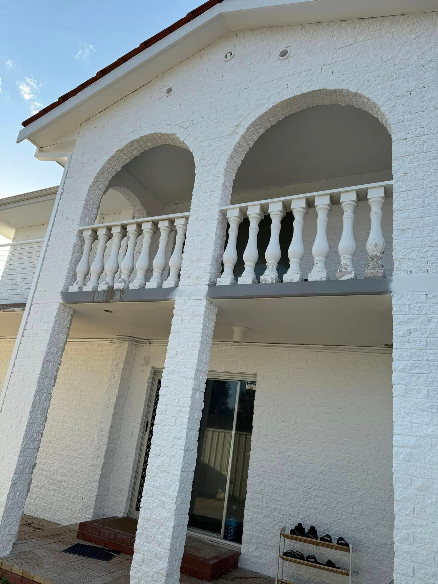 White stucco house with arched balcony, balustrade railing, and glass door.
