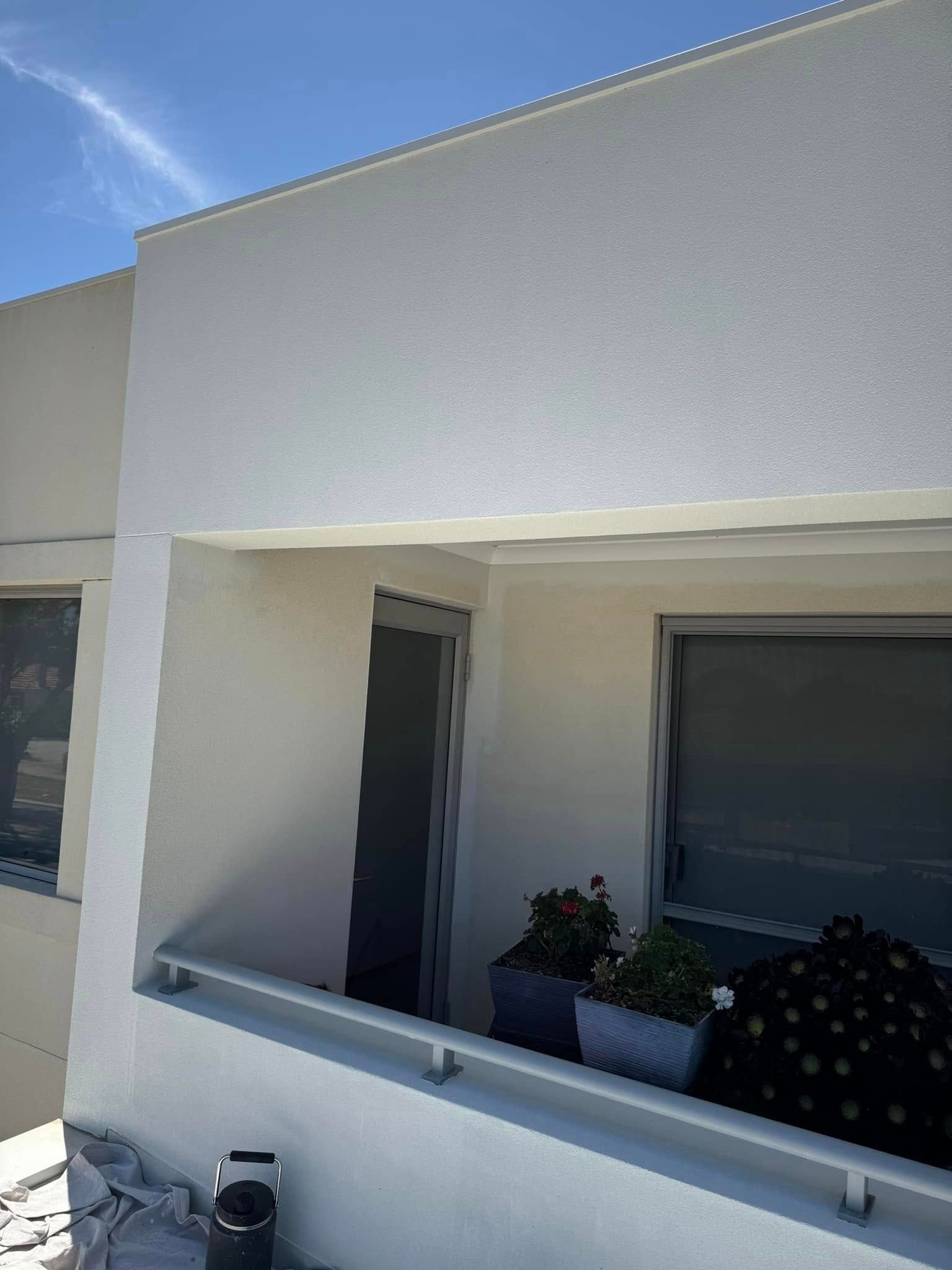 White stucco building exterior with a balcony, potted plants, and windows.