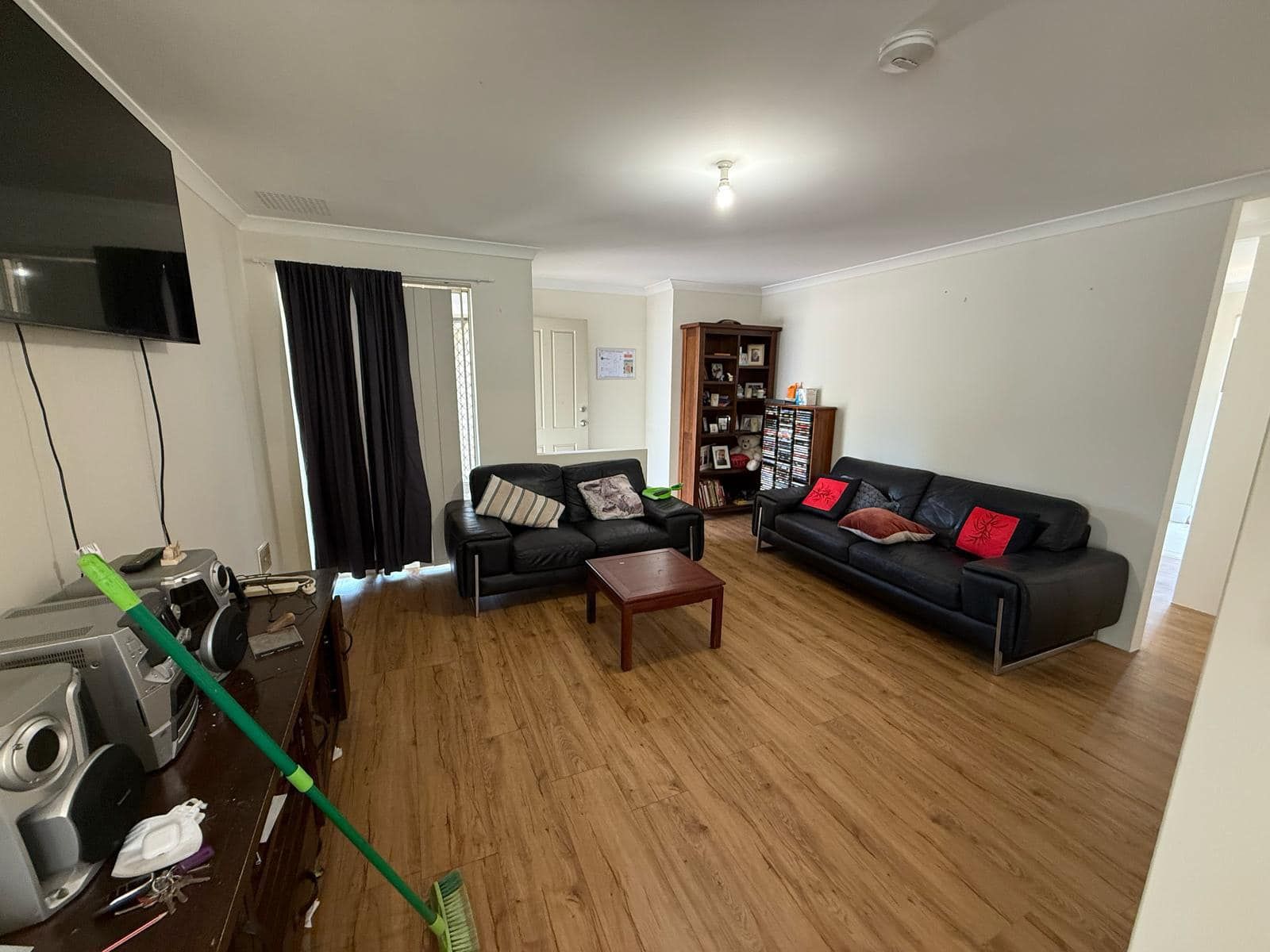 Living room with black leather couches, coffee table, wood floor, and bookcase.