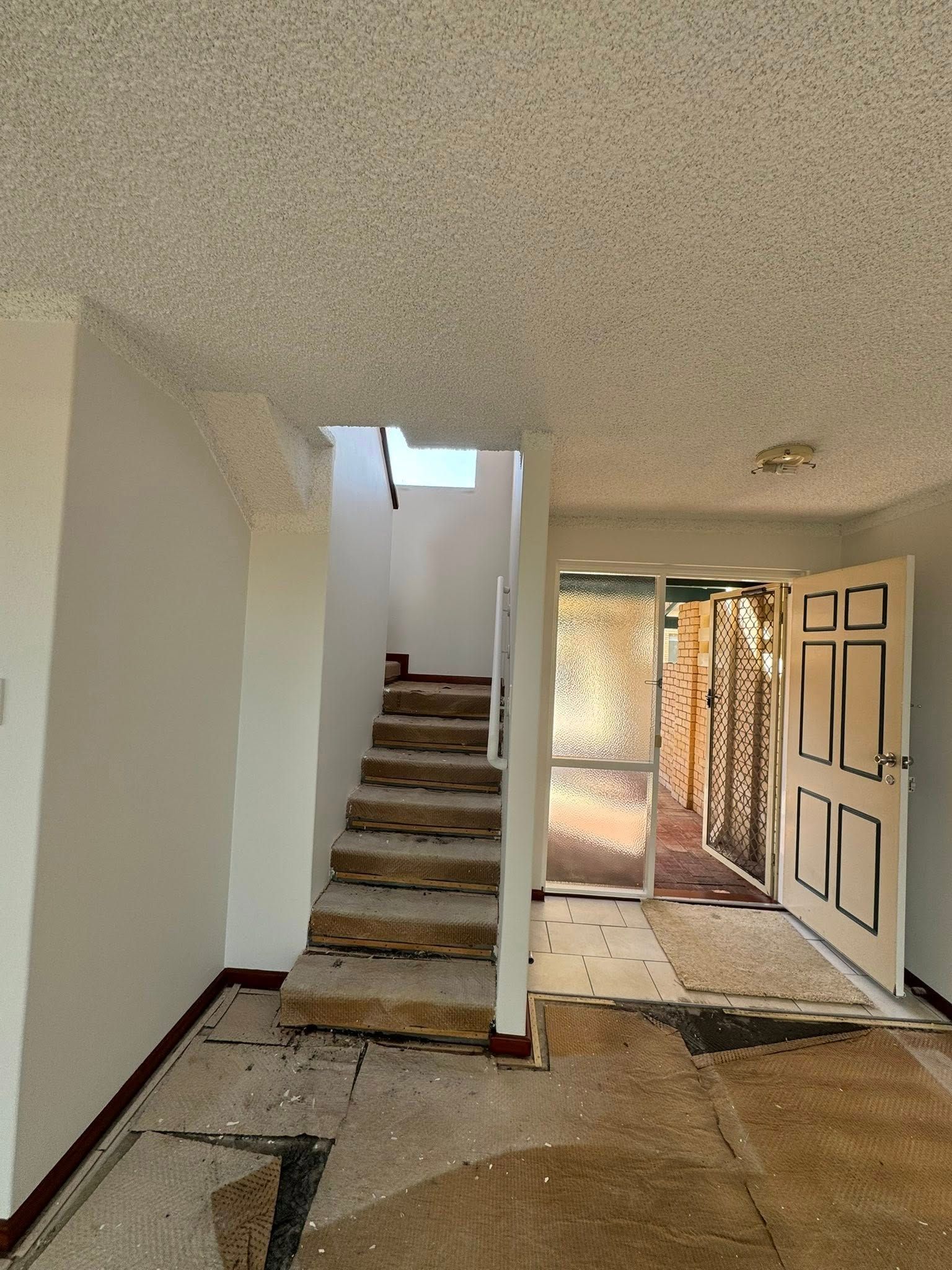 Interior view of a building's entrance and staircase. Open door with gate leads outside. Stairs going up.