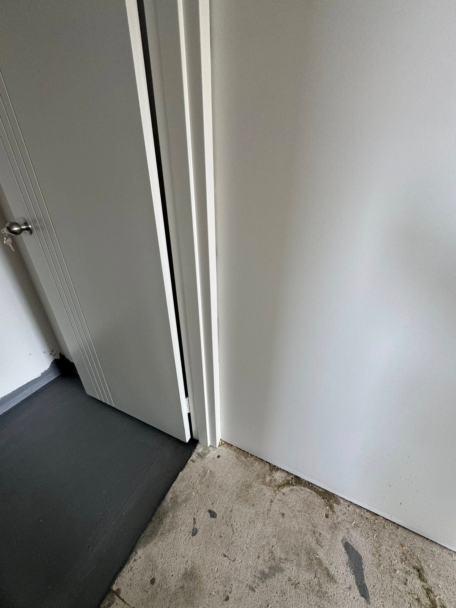 Gray door slightly ajar against a white frame; visible concrete and dark flooring.