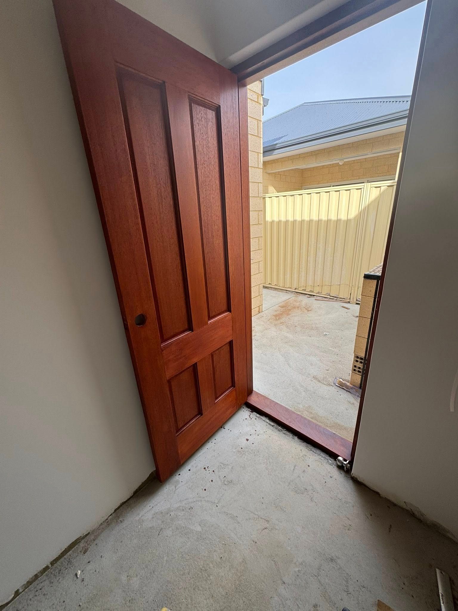 Wooden door, partially open, revealing outdoor scene with a fence.