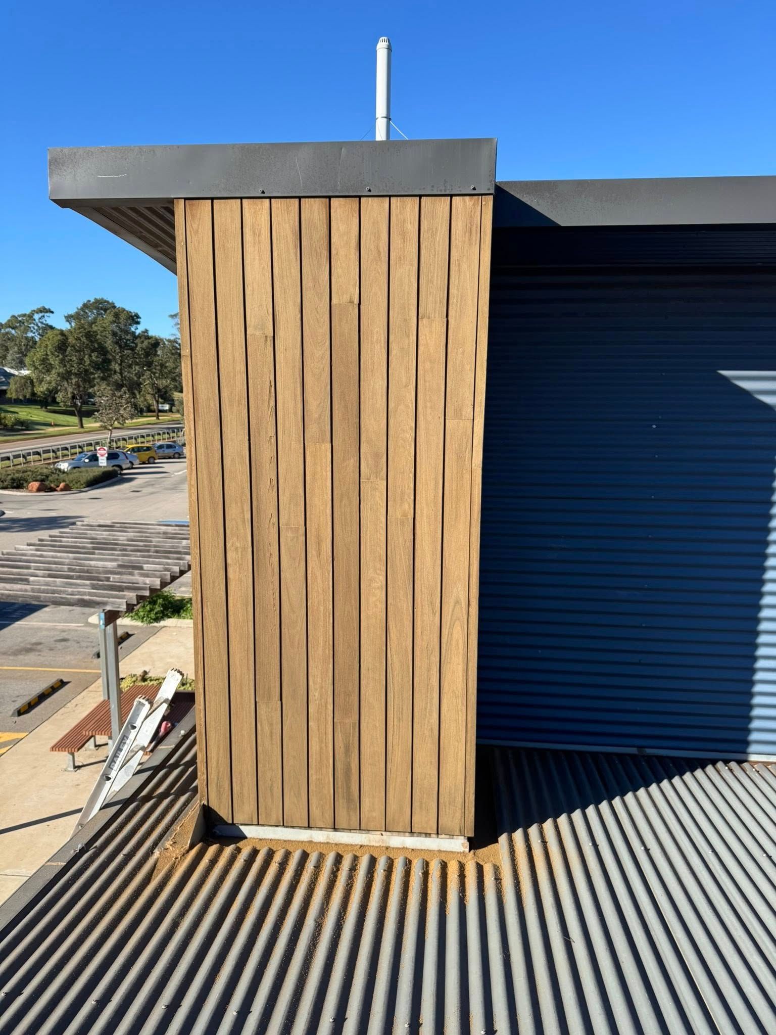 Wooden pillar with textured vertical strips, on a corrugated roof next to a blue wall. Bright sunlight.