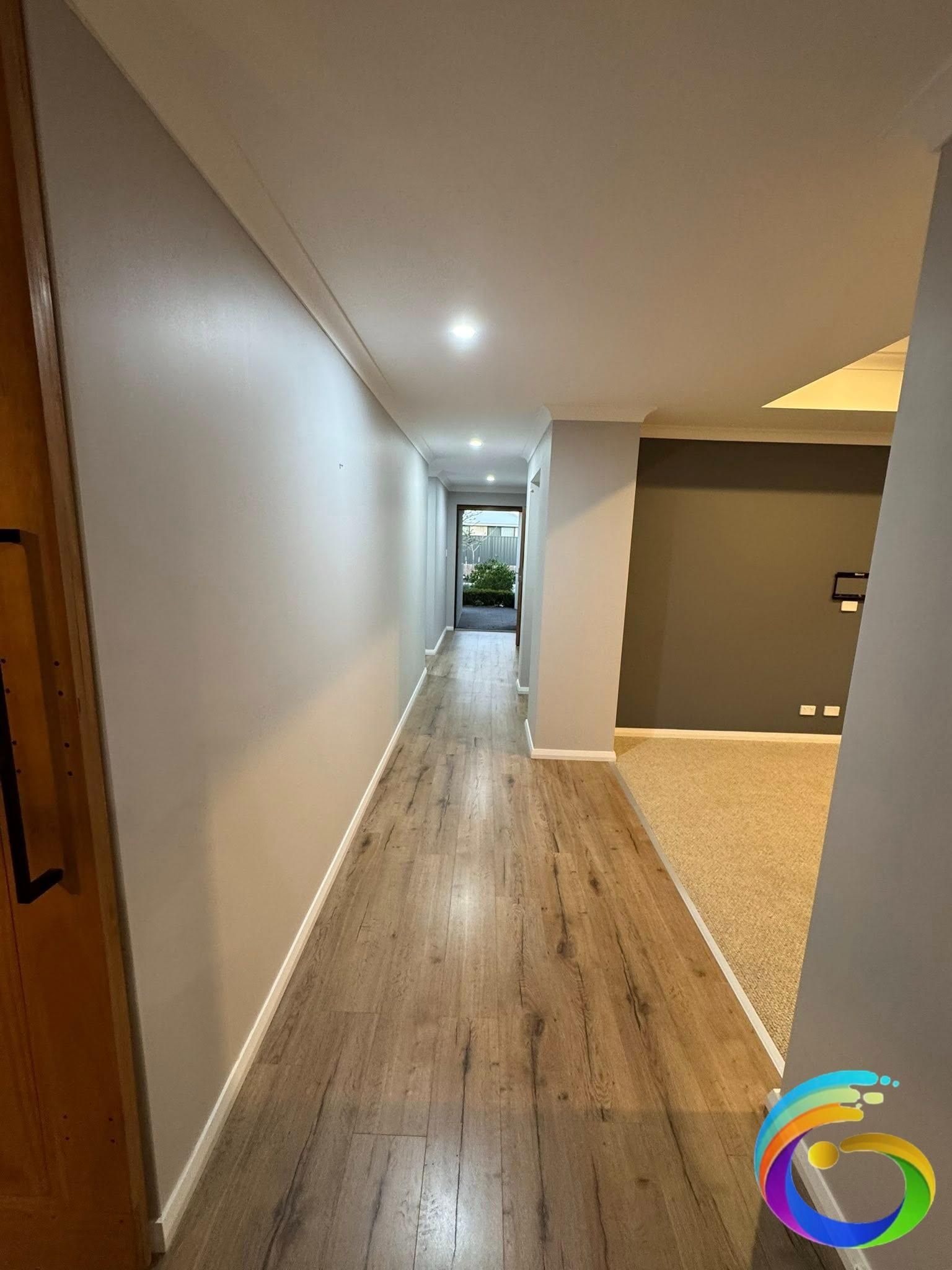 Long, narrow hallway with wood-look flooring, light gray walls, and recessed lighting.