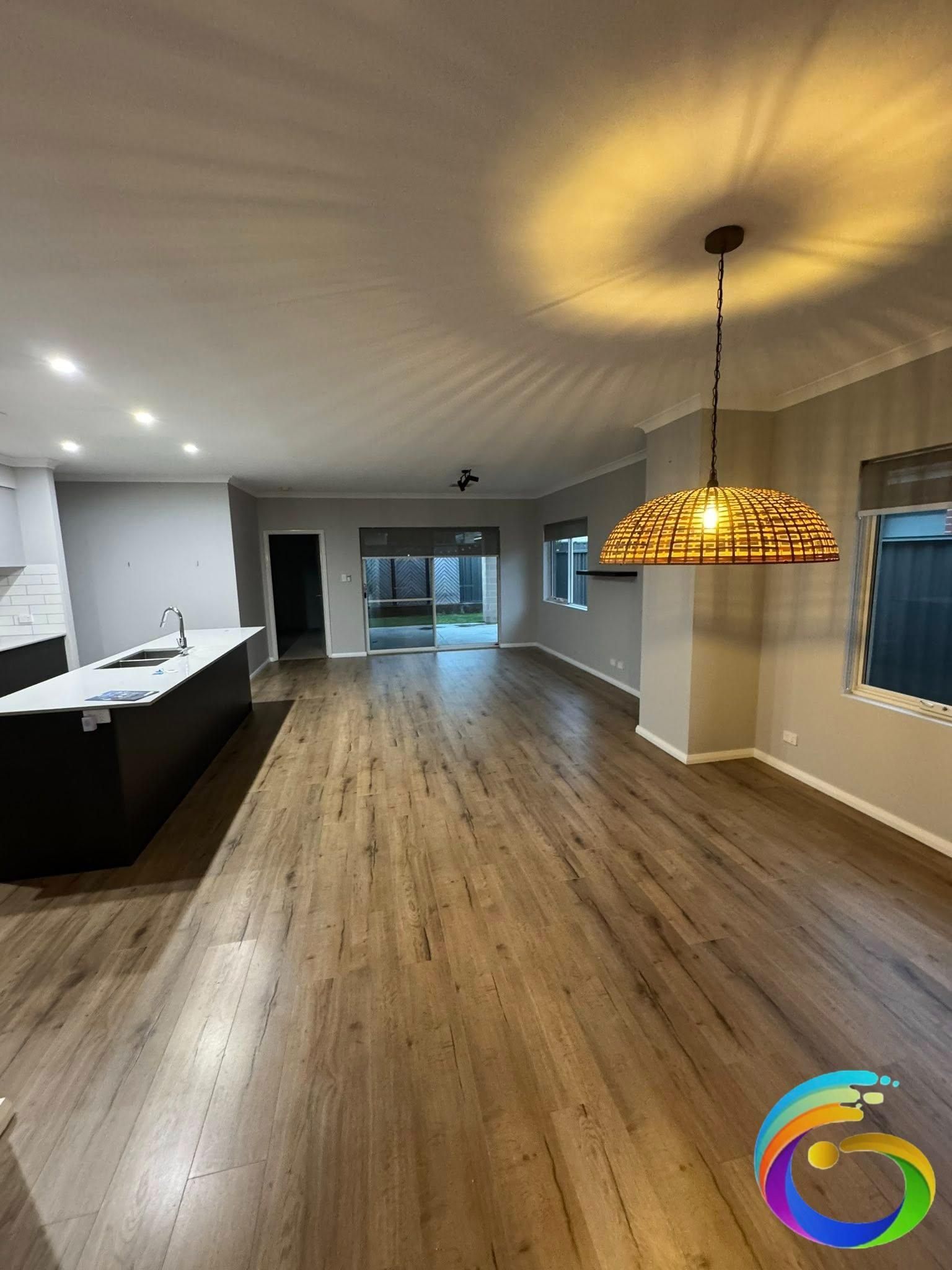 Spacious open-plan interior with wooden floors, kitchen island, and a light fixture hanging from the ceiling.