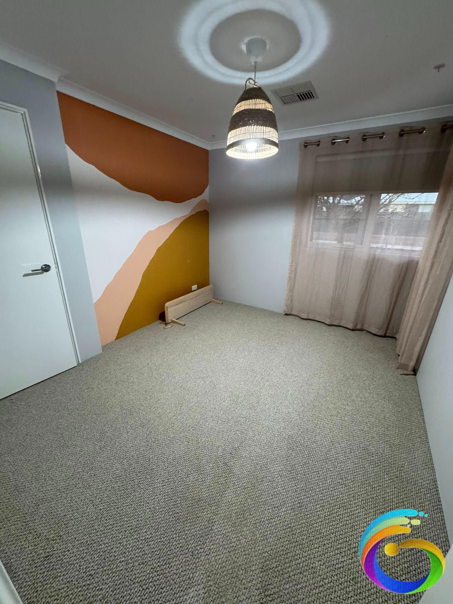 Empty bedroom with patterned carpet, decorative wall paint, and a hanging light fixture.