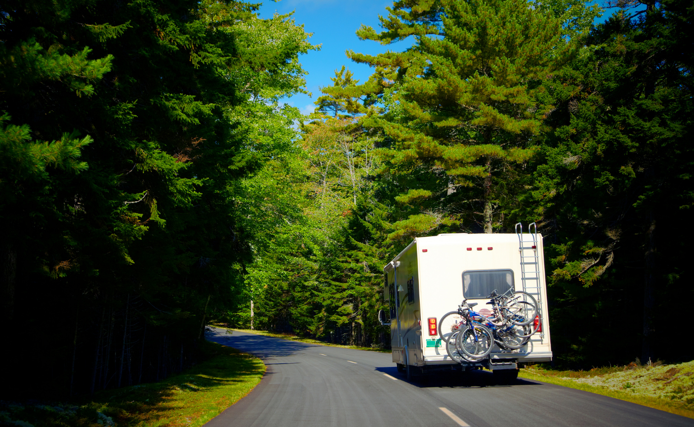 A white rv with bikes on the back is driving down a road.