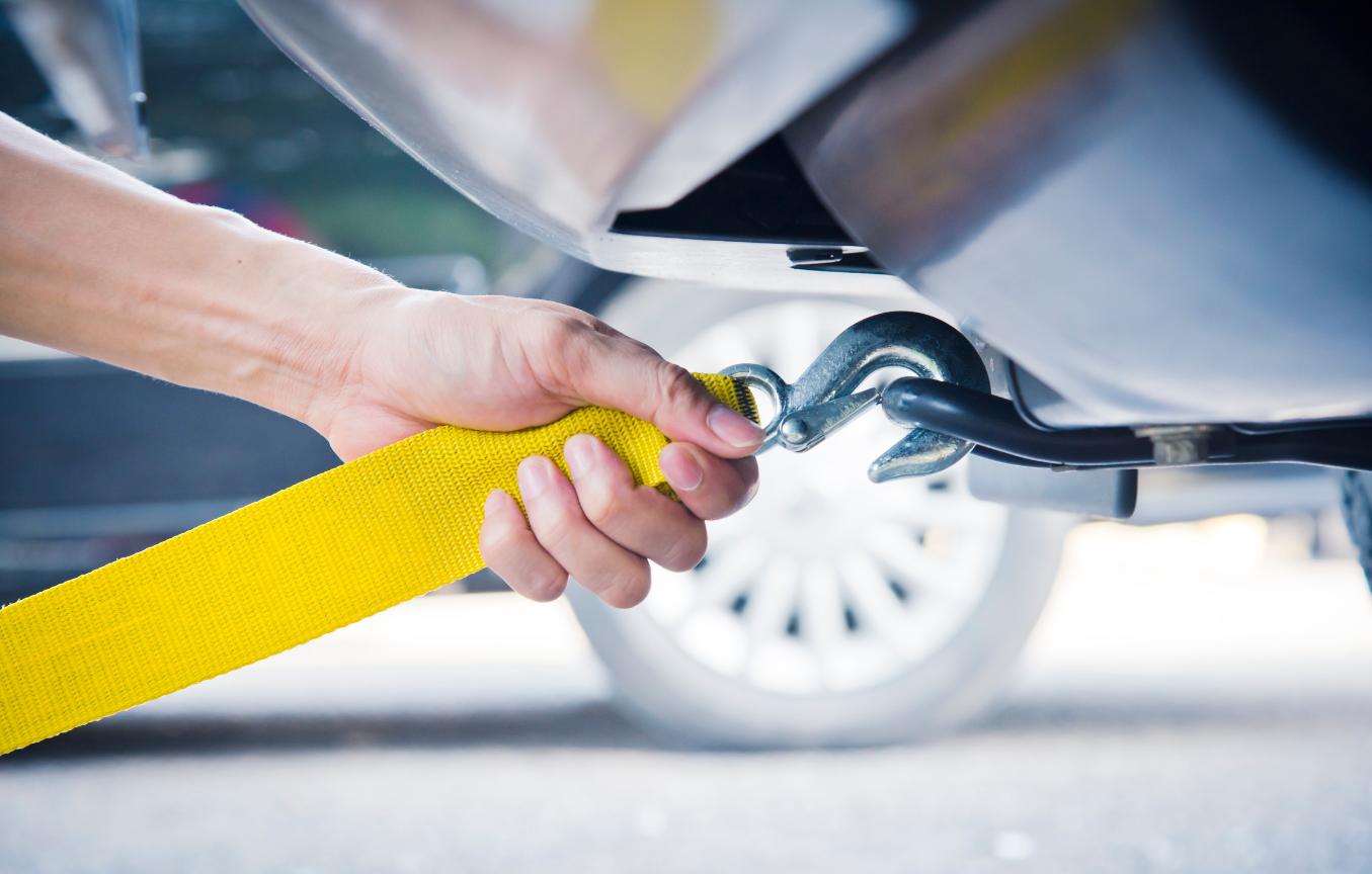 A person is towing a car with a yellow tow strap.