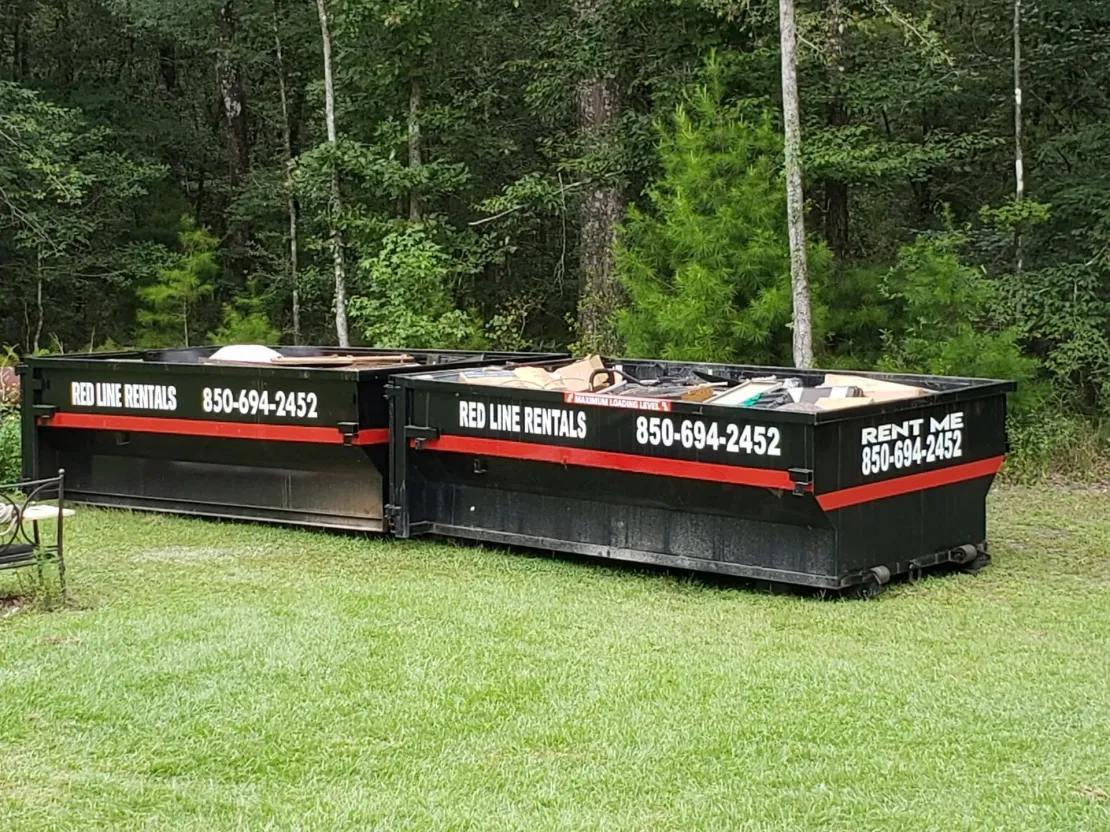 Two black dumpsters on grass, labeled 