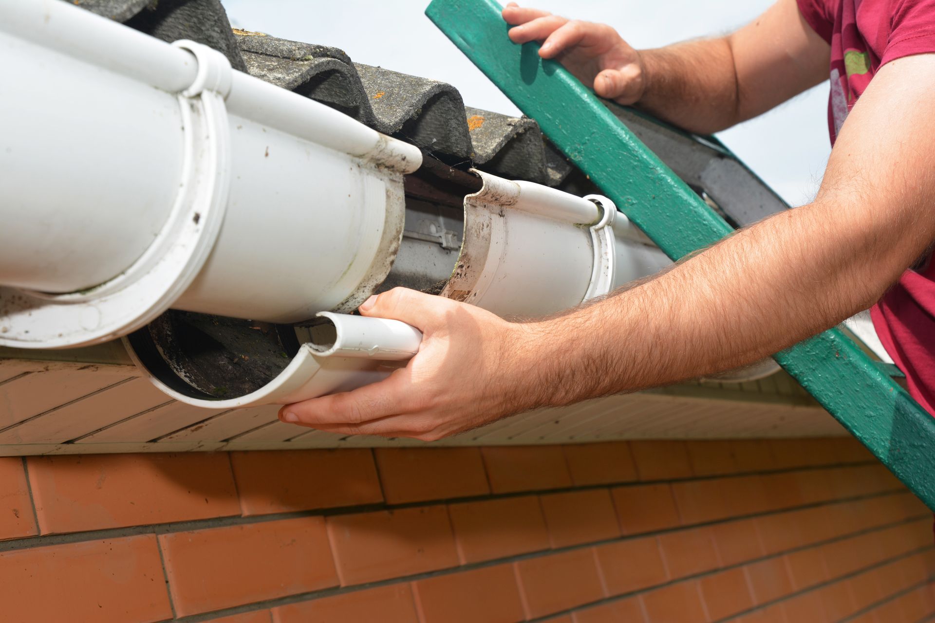 Person installing gutter guard on white gutter against a red brick building.