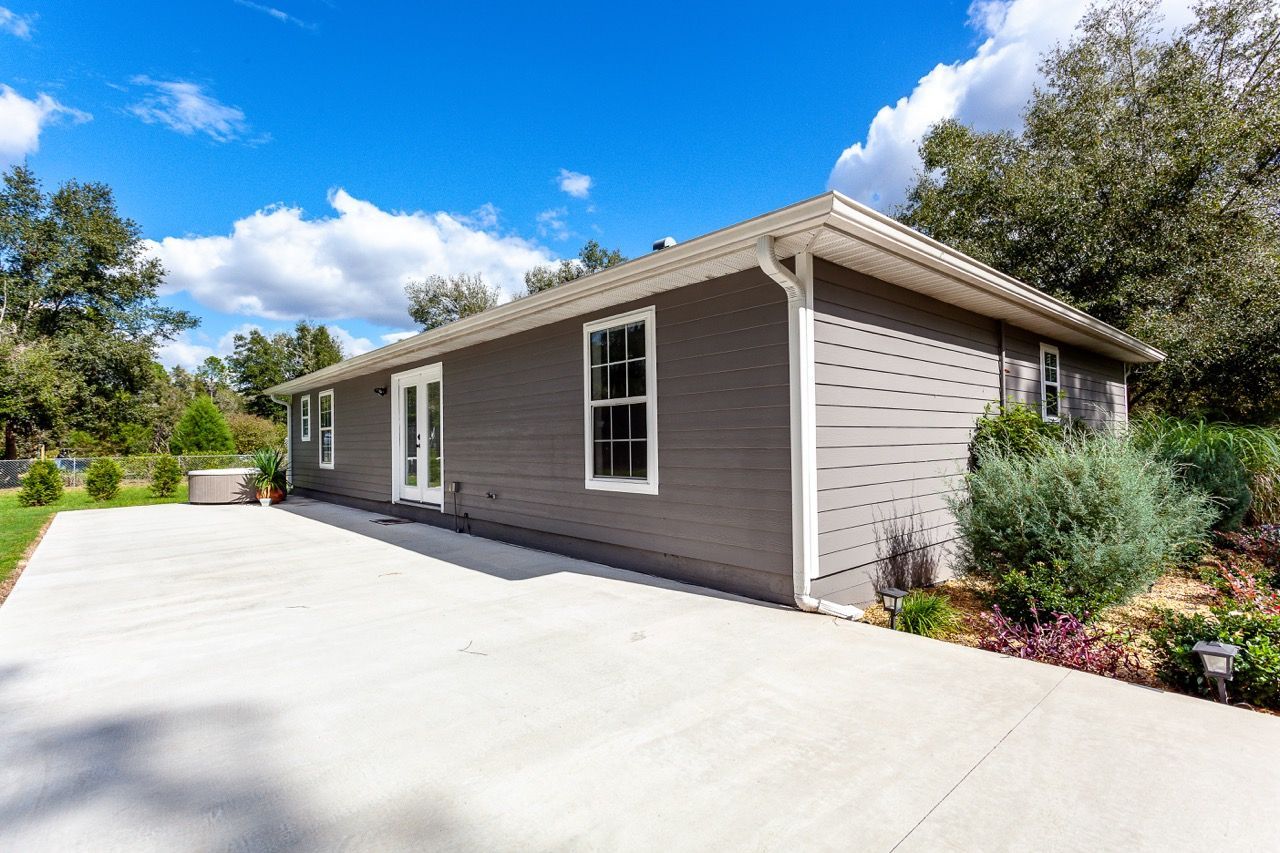 Rainwater streams from a rusty gutter on a brick building, a house in the background.