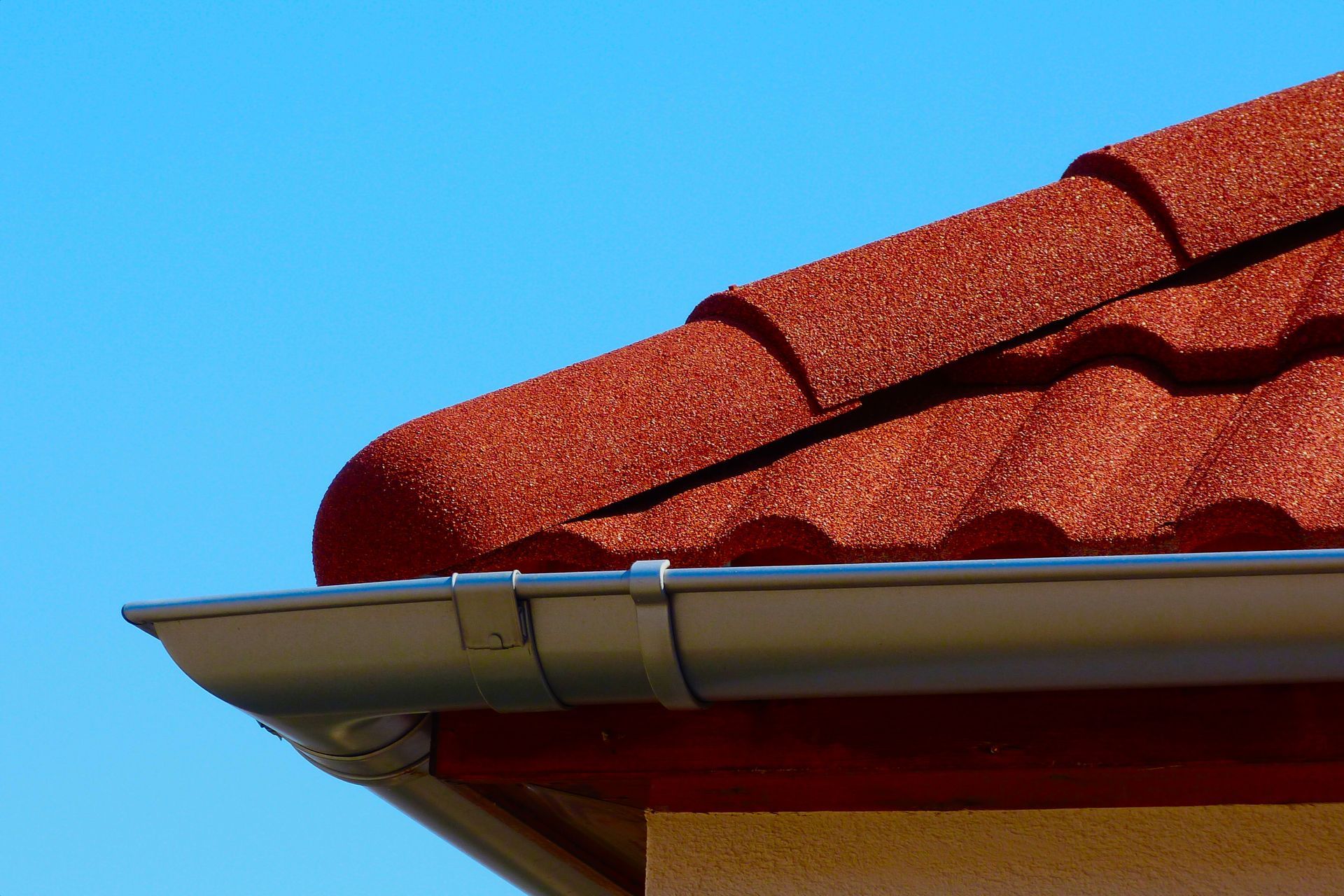Red tile roof with silver gutter against a clear blue sky.