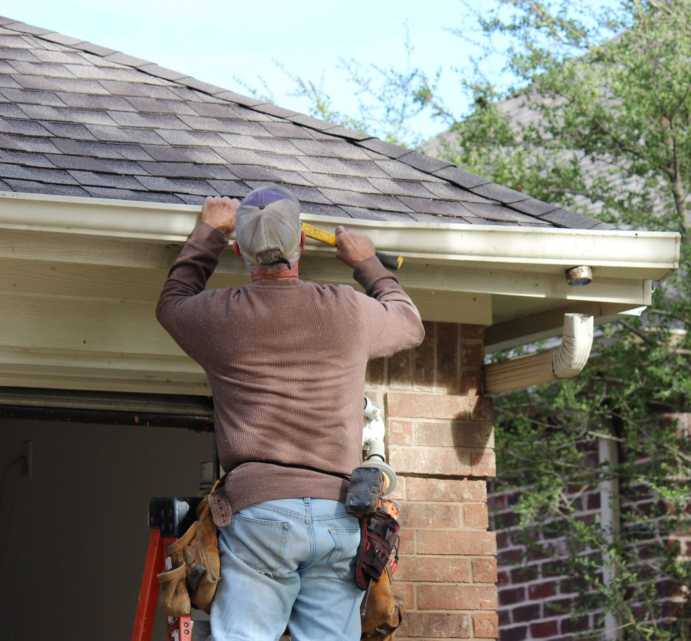 Person on ladder installing gutter on a brick house.