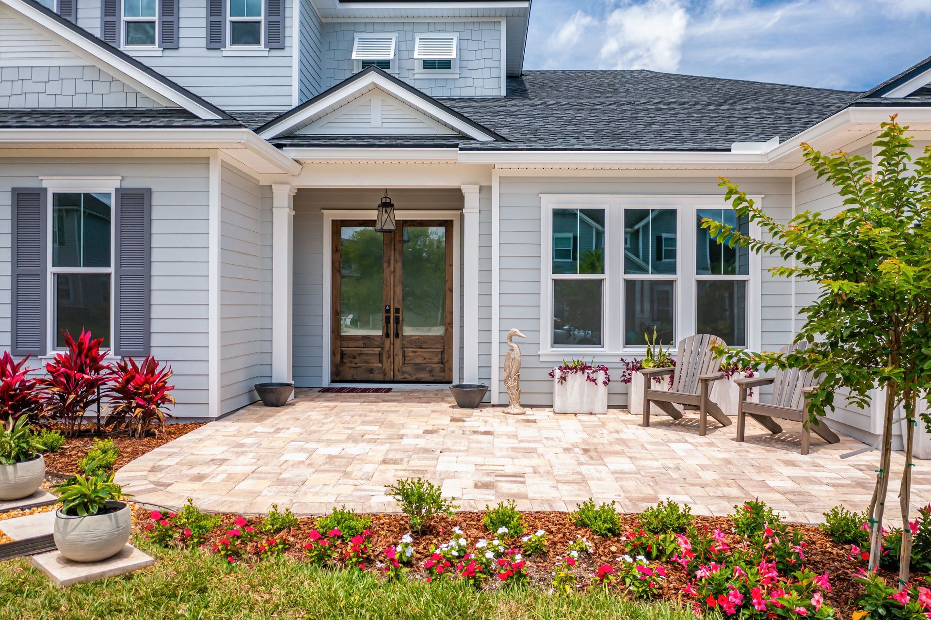 Man on a ladder cleaning a roof gutter of leaves. He is wearing a black jacket and cap.