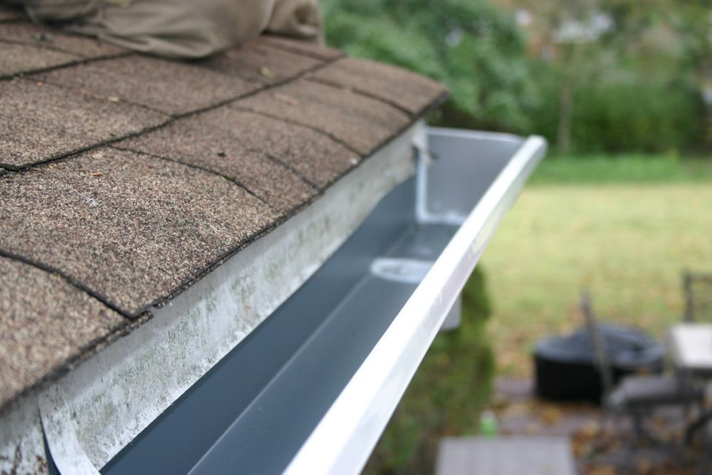 Gutter along a shingled roof edge with water channeling toward the downspout
