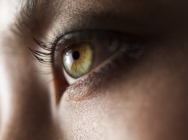 Close-up of a person's eye, showing a green iris with a black pupil, and long eyelashes.
