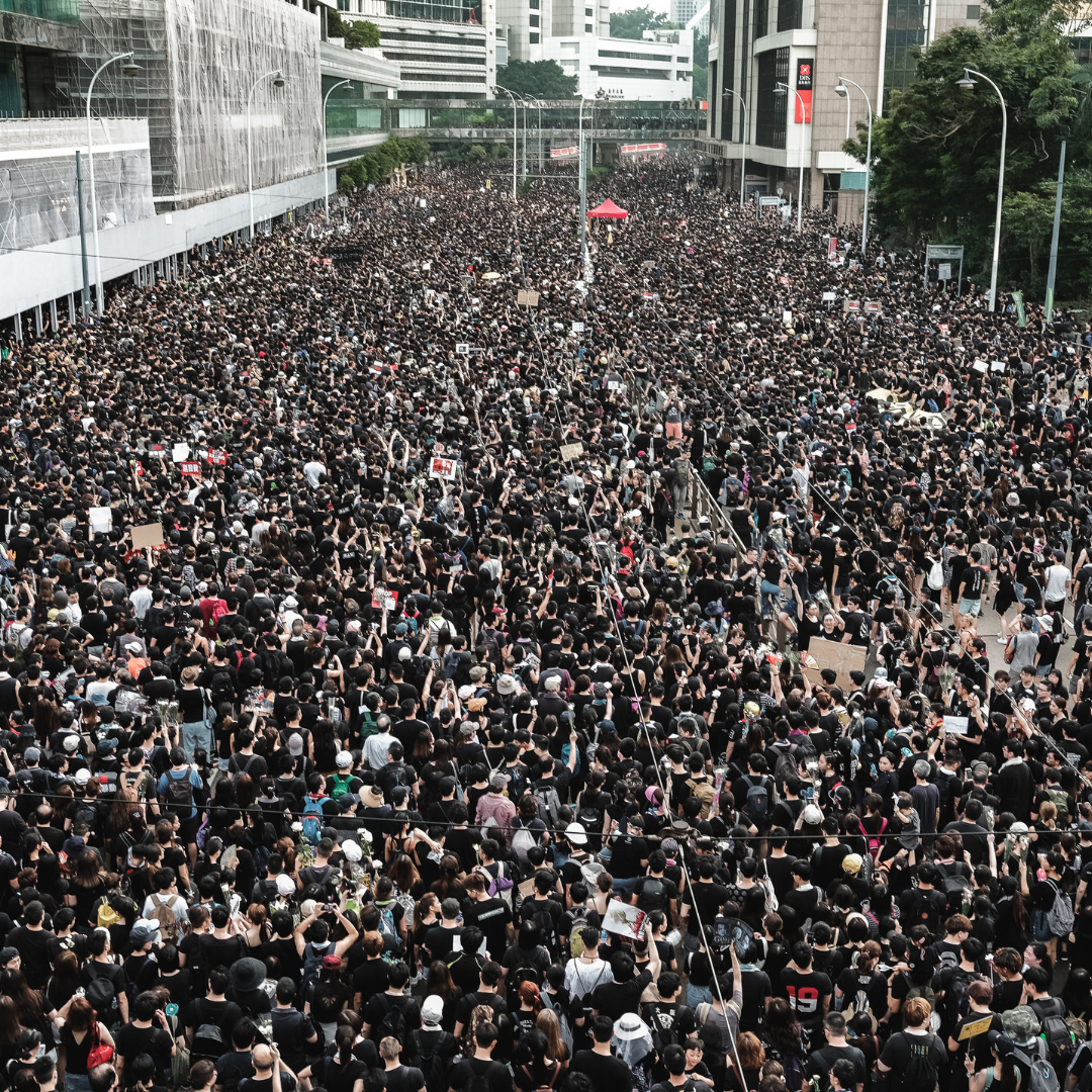 Large crowd of people, mostly in black, filling a city street, possibly a protest.