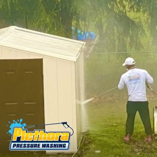 A man is using a pressure washer to clean a shed.