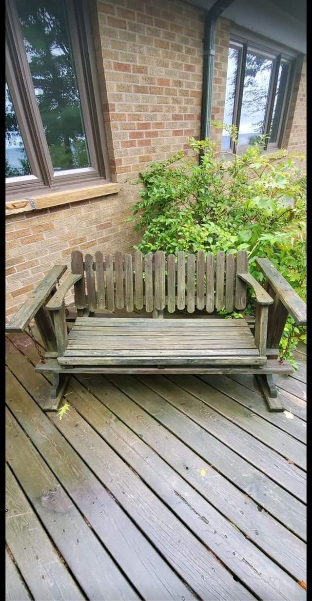 A wooden bench is sitting on a wooden deck in front of a brick building.