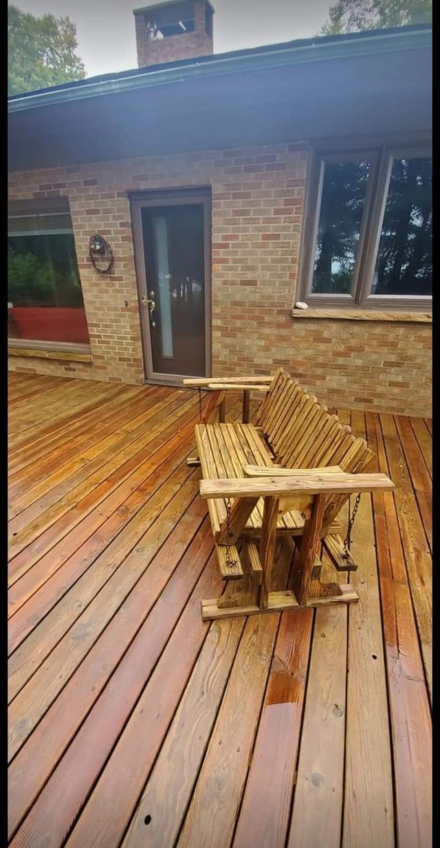 A wooden deck with two wooden chairs on it in front of a brick house.