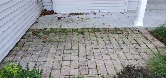 A brick patio with grass growing on it in front of a house.