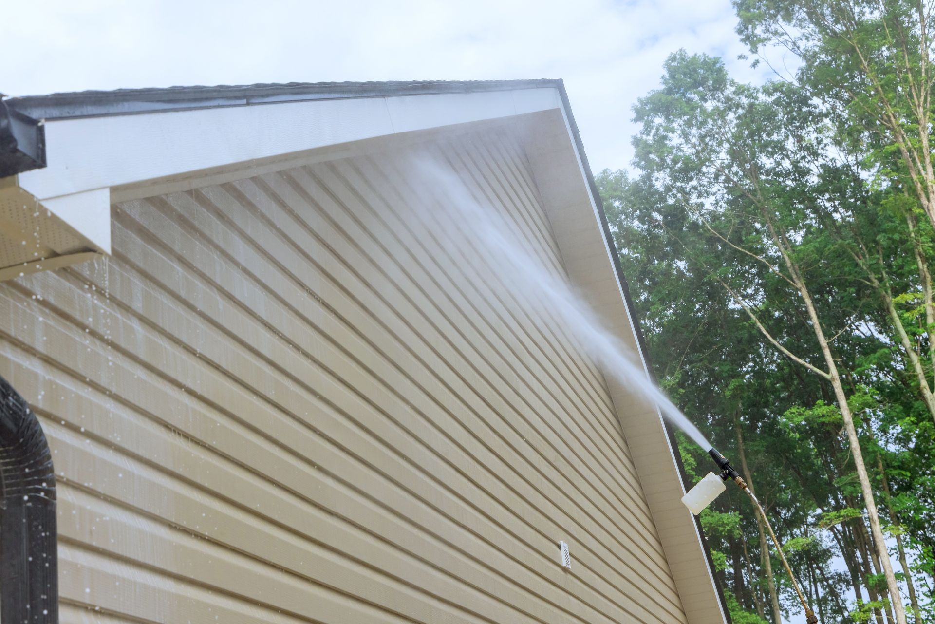A person is using a high pressure washer to clean the side of a house.