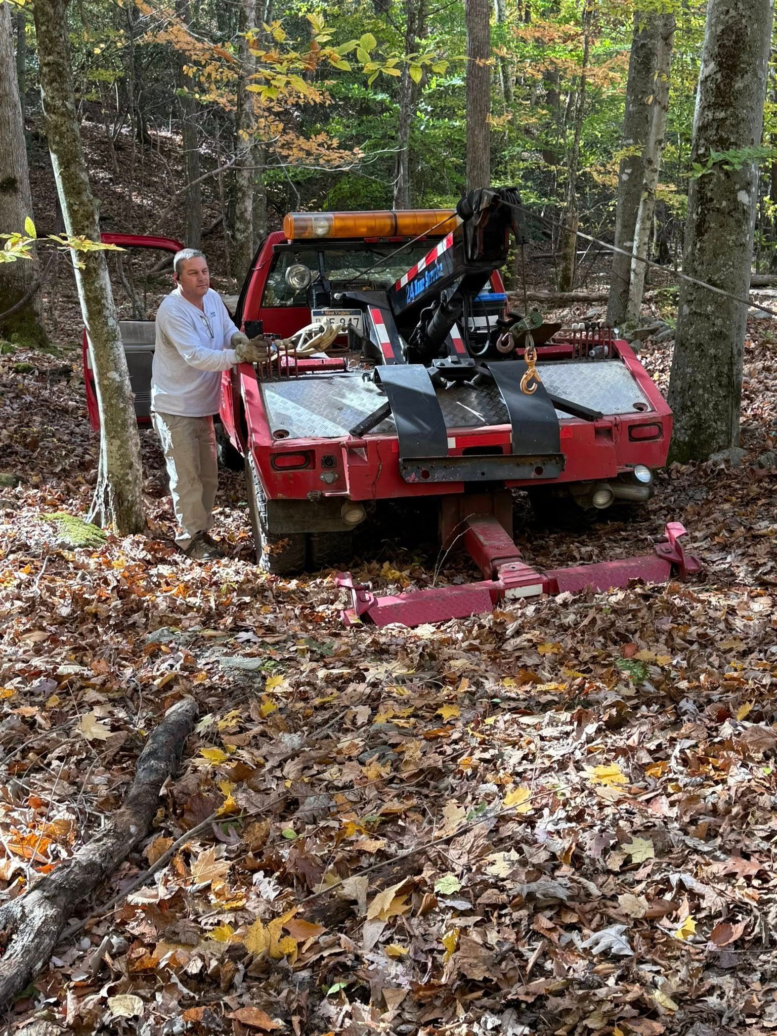 Person stands by a red off-road vehicle stuck on a forest trail in autumn leaves.