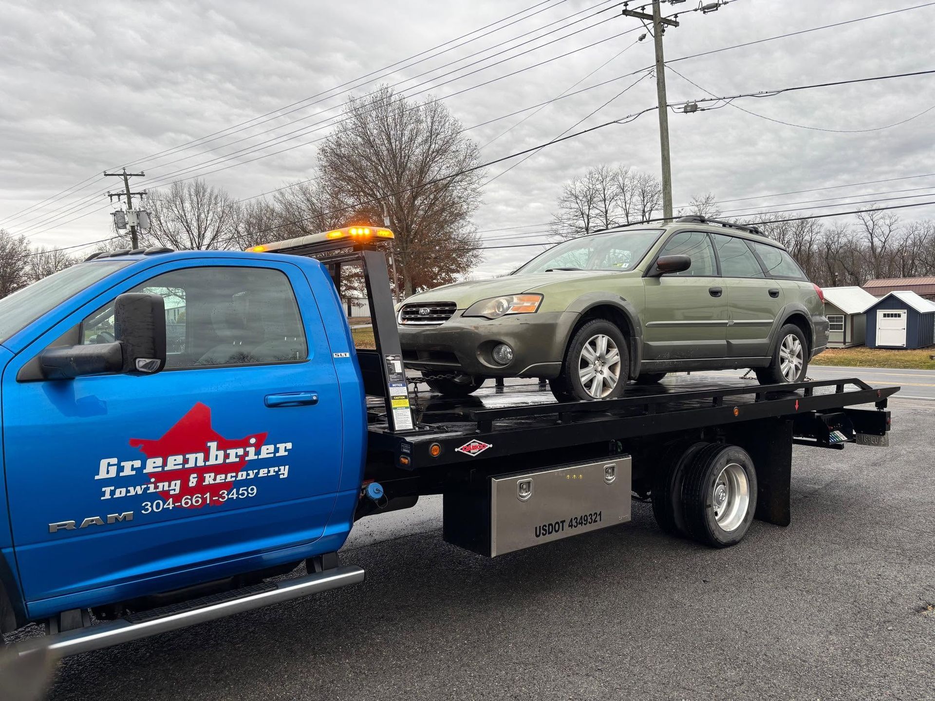 Blue tow truck hauling a green SUV on a flatbed in a cloudy roadside setting