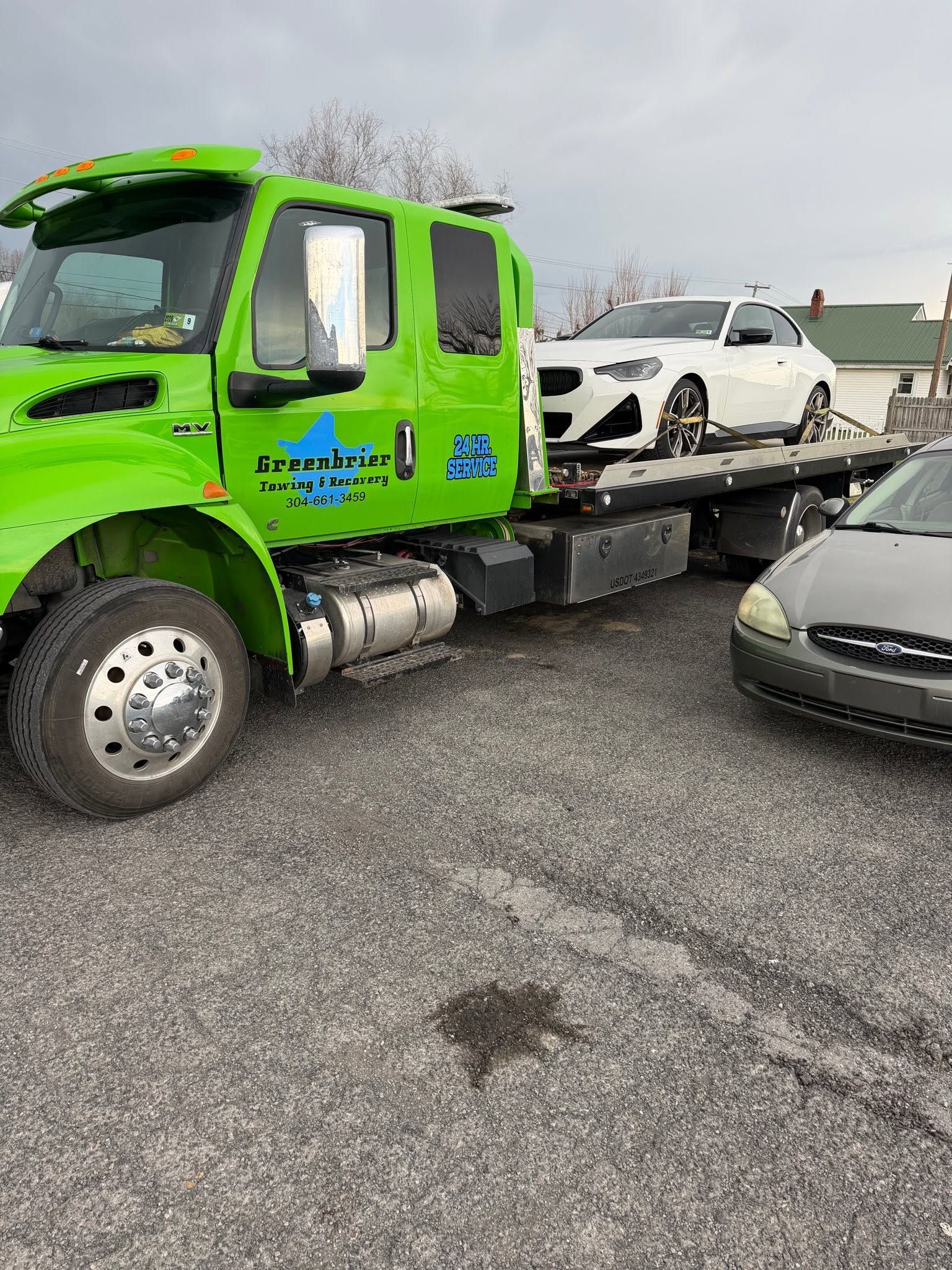 Bright green flatbed tow truck carrying a white SUV in a parking lot with a gray car nearby