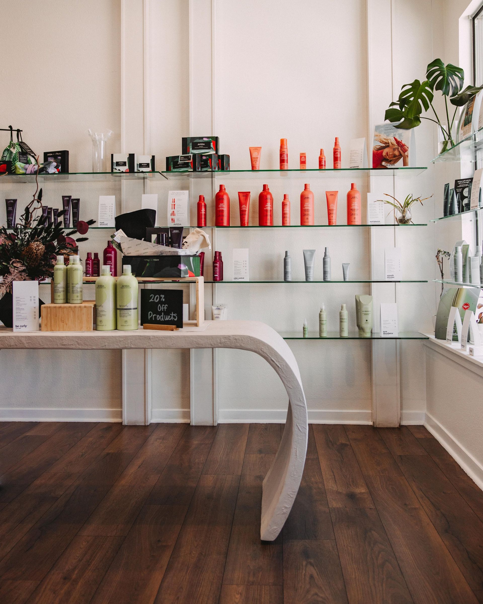 Hair salon interior with products on display shelves, curved white table, and wooden floor.