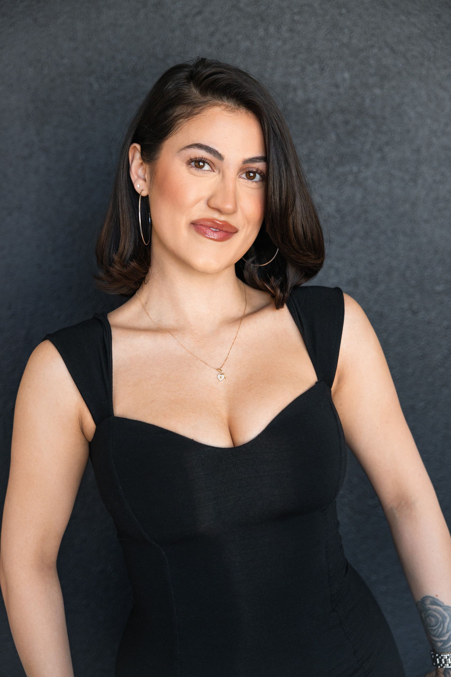 Woman with dark hair in a black dress smiling at the camera against a dark backdrop.