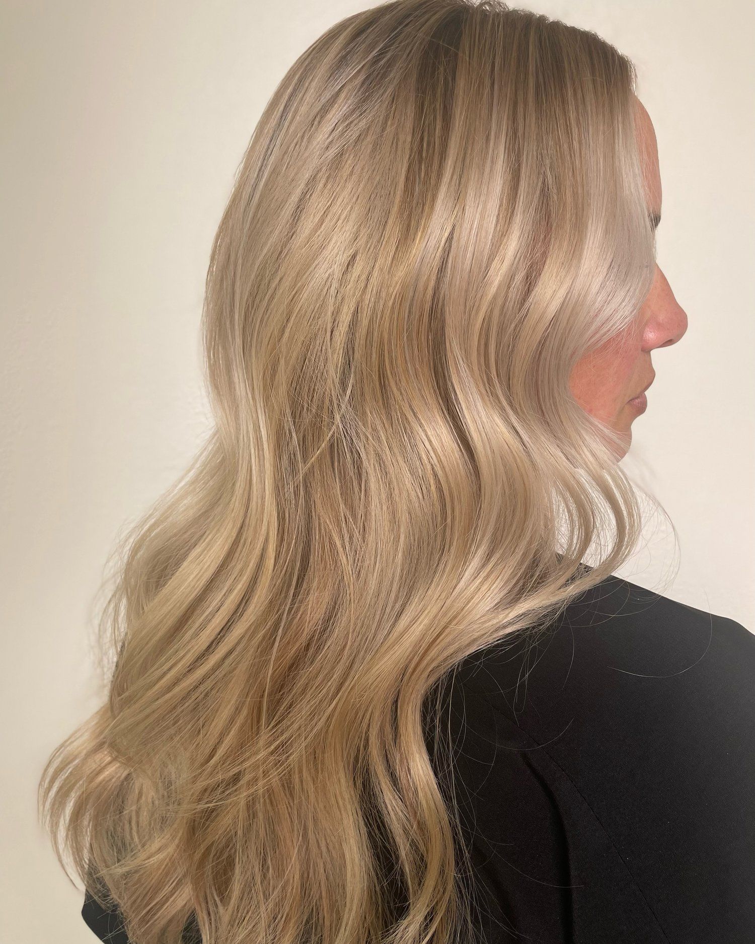 Woman with long, wavy, blonde hair, wearing a black top, turned in profile against a white background.