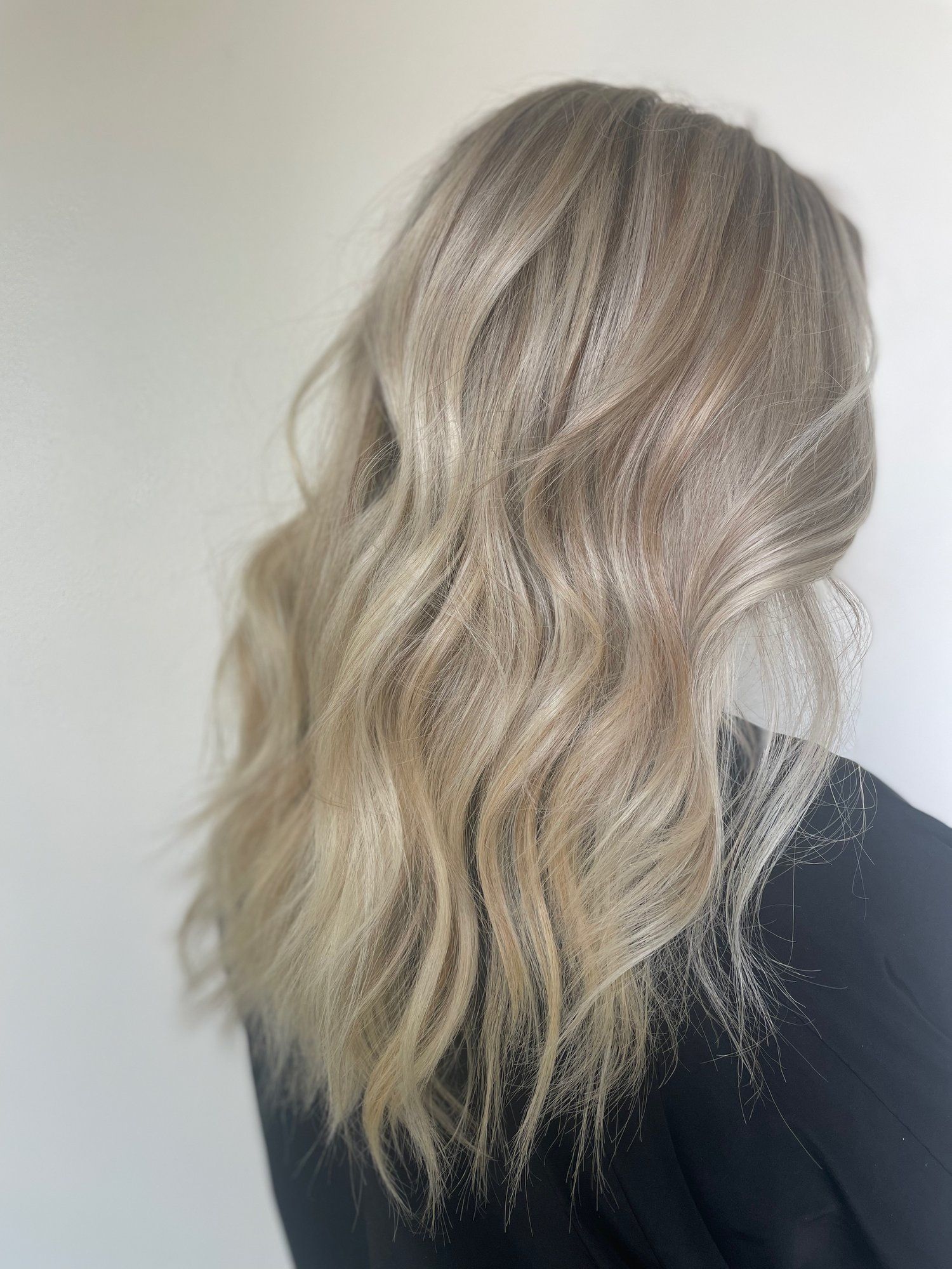 Woman with wavy, blonde balayage hair against a white background, viewed from the side.