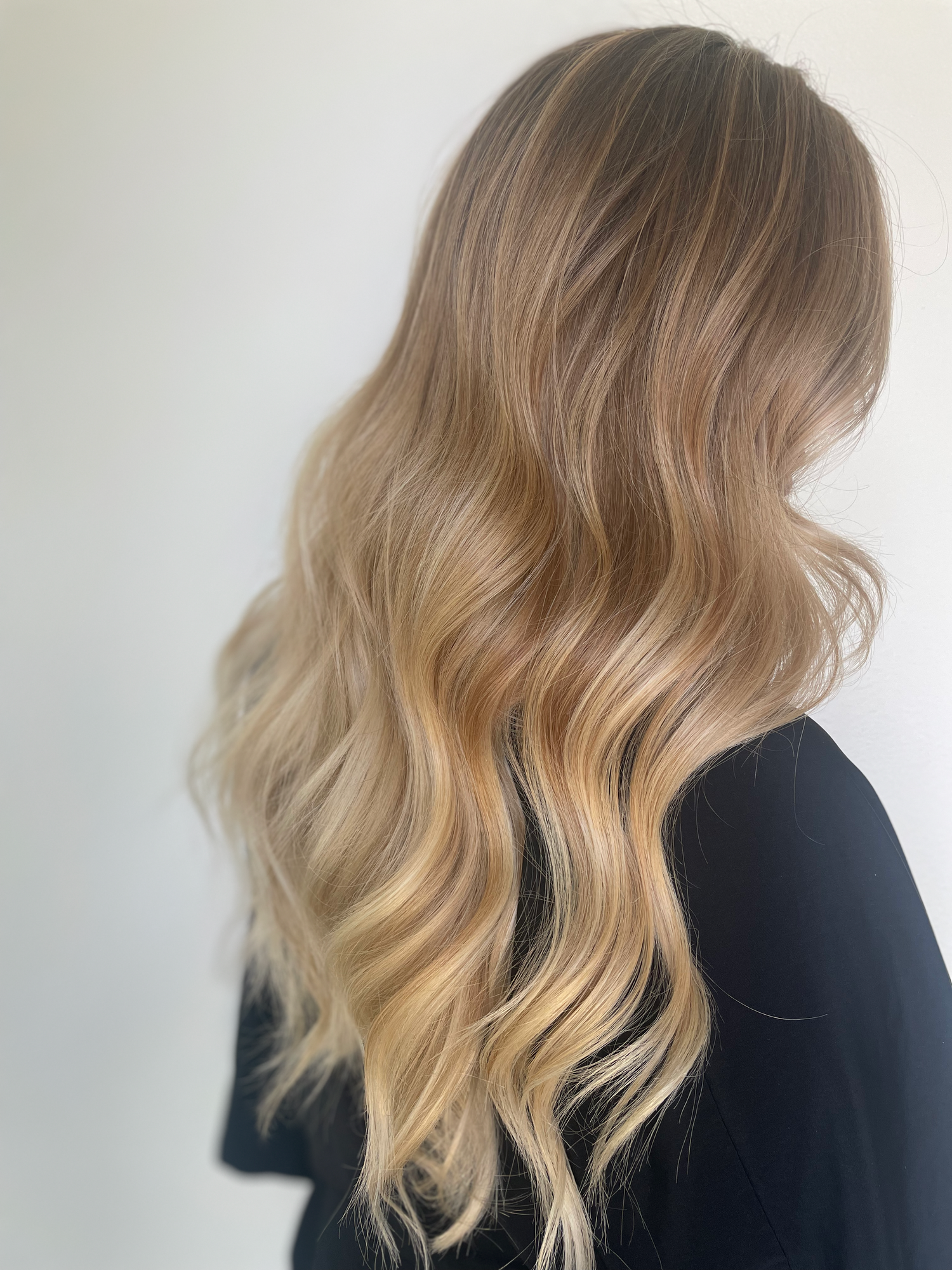Woman with long, wavy hair, transitioning from darker blonde at the roots to lighter blonde ends, against a plain white background.