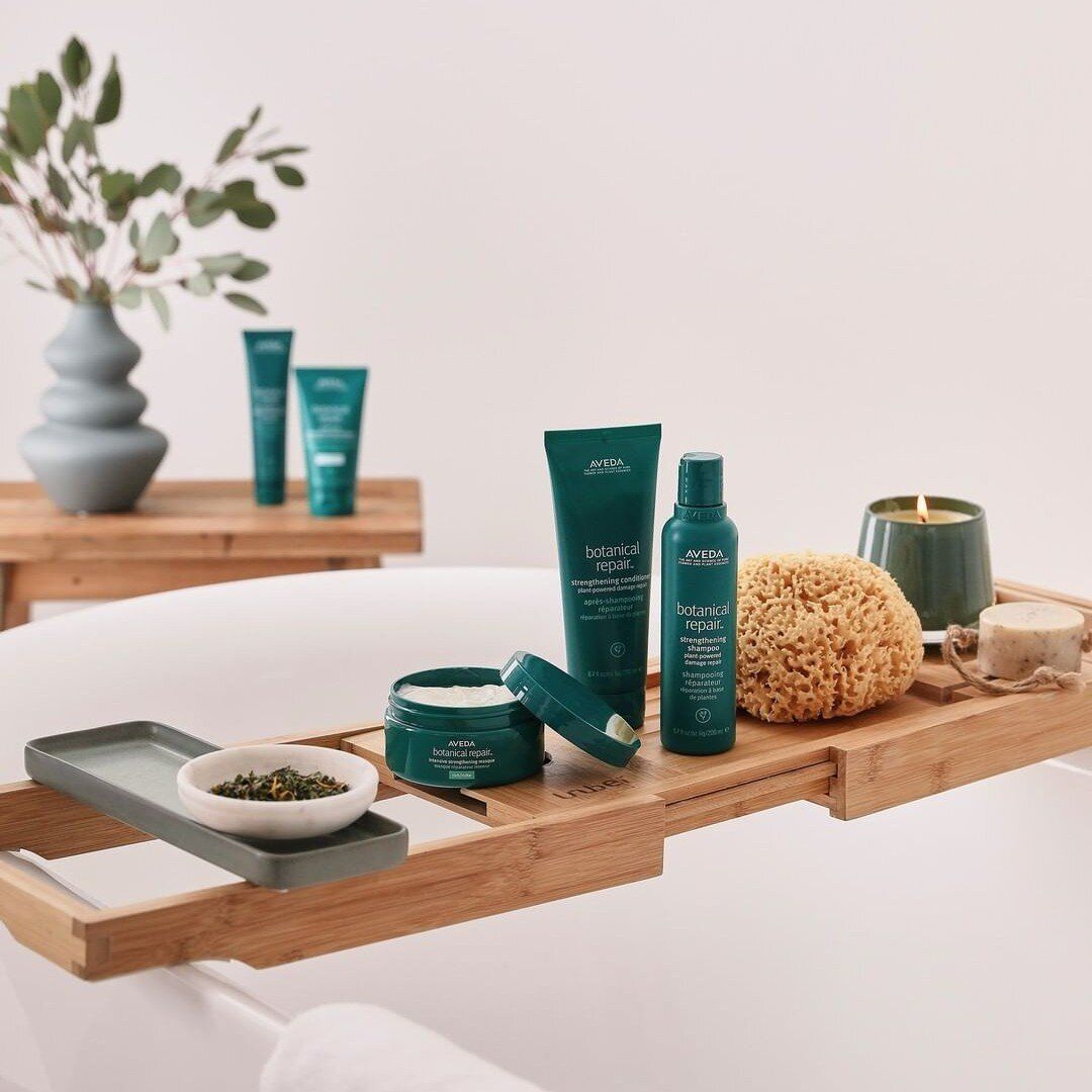 A spa-like setup with bath products on a bamboo tray over a bathtub. Products are in teal bottles and jars, with a candle and sponge.